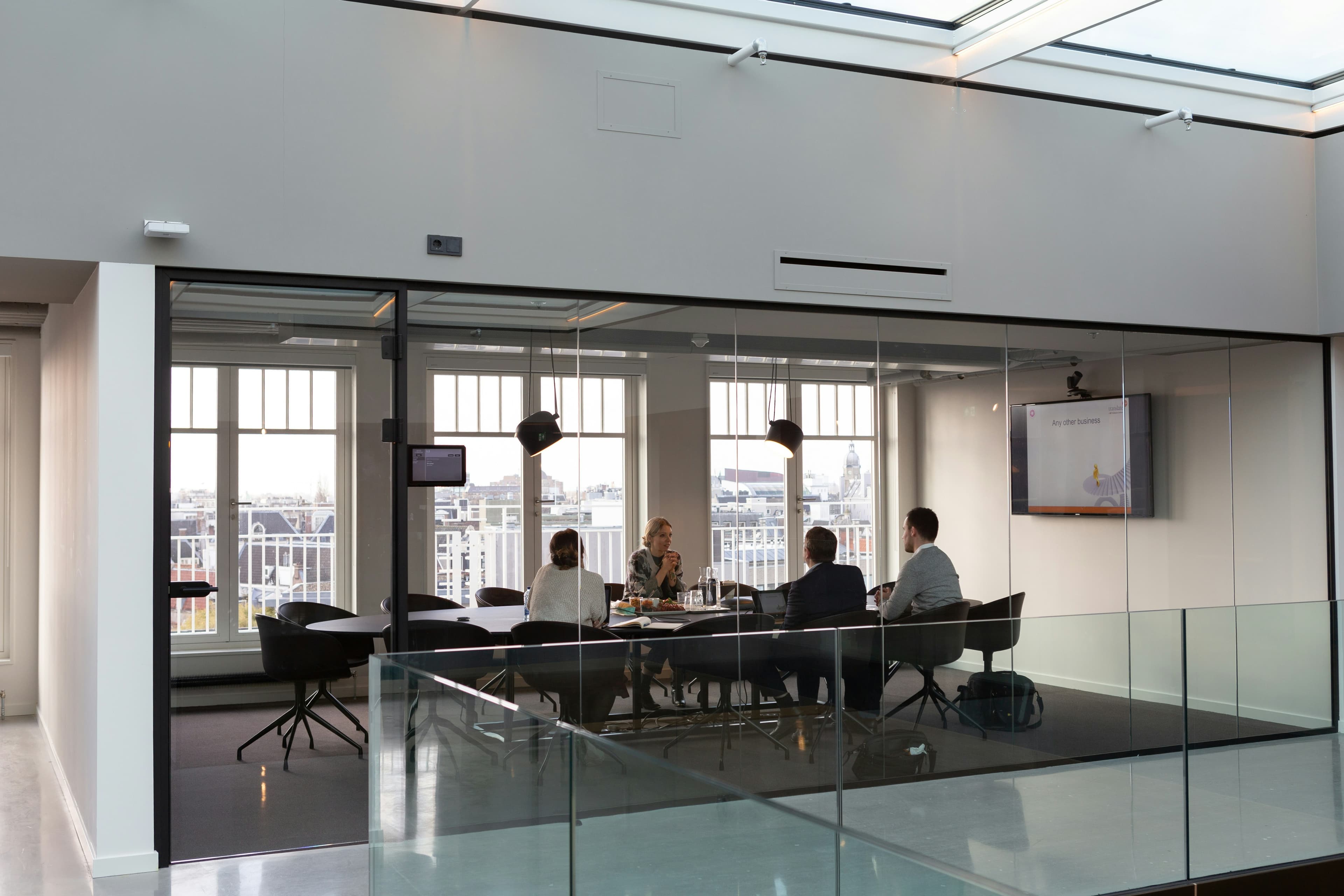 Four colleagues in a meeting around a boardroom table, seen through a glass wall.